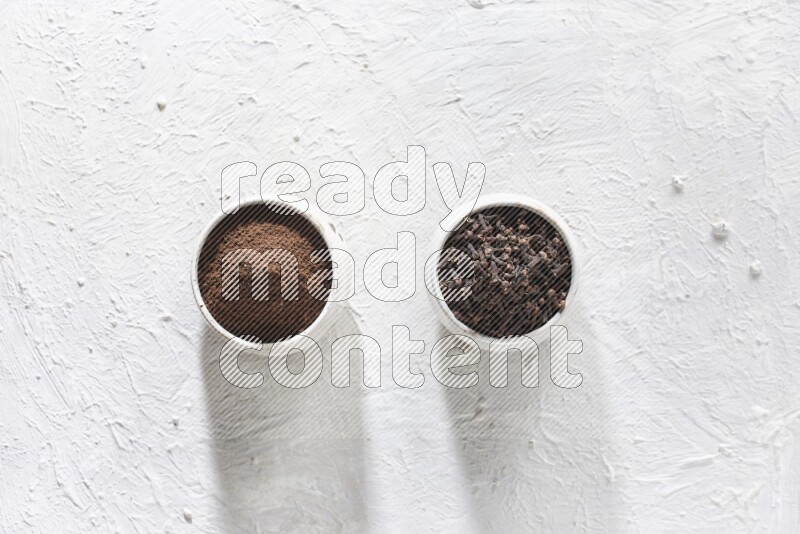 2 Beige ceramic bowls, one full of cloves and the other full of powder on textured white flooring
