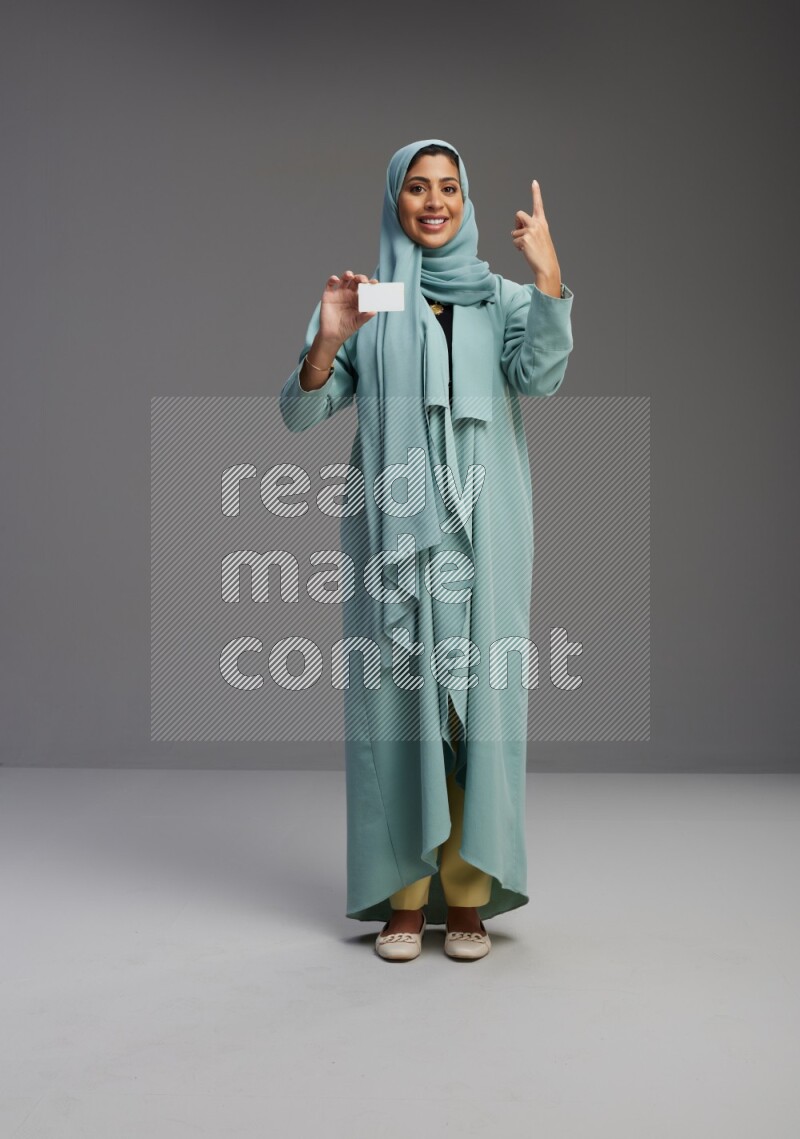 Saudi Woman wearing Abaya standing holding ATM card on Gray background