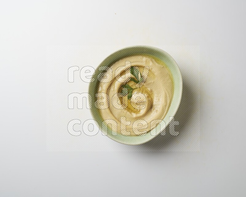 Hummus in a green plate garnished with parsley on a white background