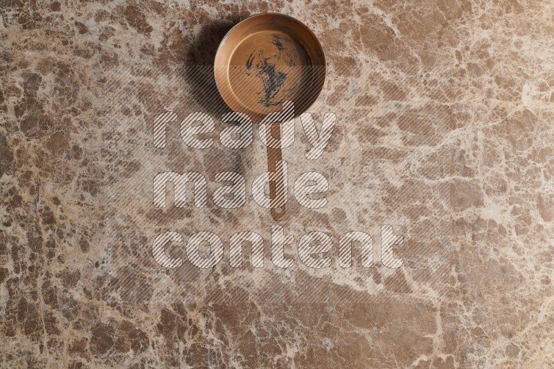 A small copper pan on beige marble background