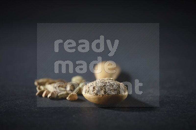 ملعقة خشبية ممتلئة ببودرة الهيل وحبوب الهيل بجانبها على خلفية سوداء