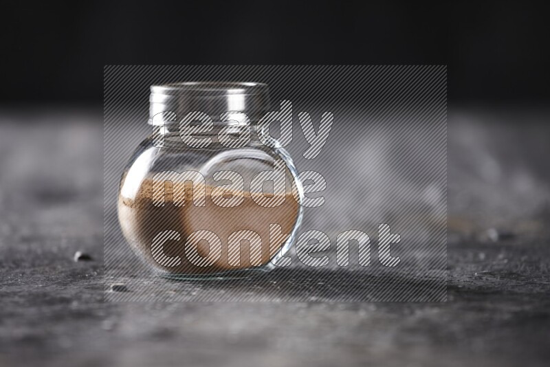 Herbal glass jar full of cinnamon powder on a textured black background
