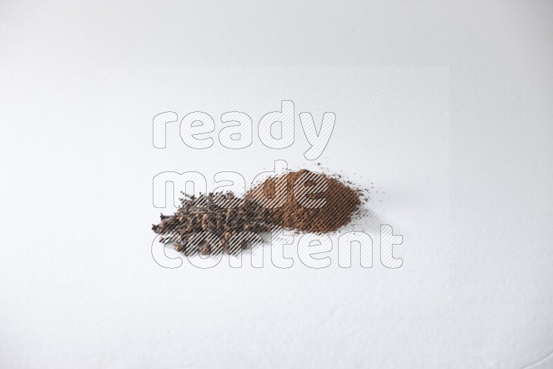 كومتان من حبوب القرنفل وبودرة القرنفل على أرضية بيضاء