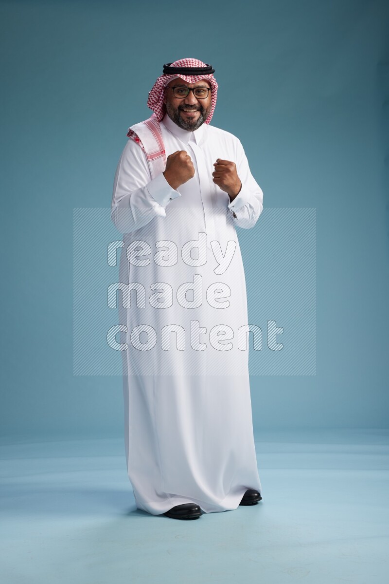 Saudi Man with shimag Standing Interacting with the camera on blue background