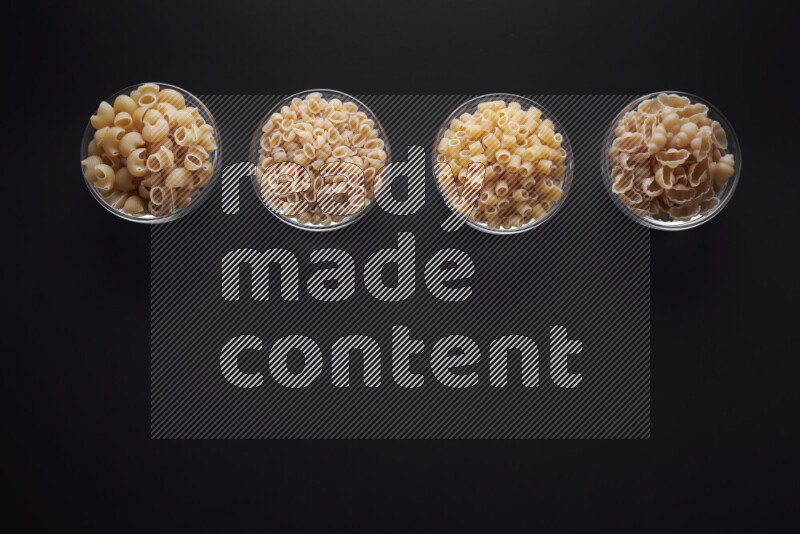 Different pasta types in glass bowls on black background
