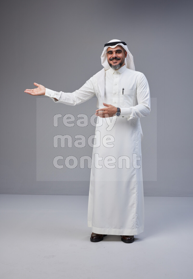 Saudi man Wearing Thob and white Shomag standing interacting with the camera on Gray background