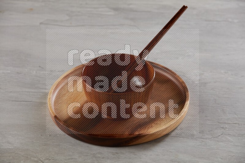brown wood round bowl on top of brown wood round plate and wood chopsticks, on grey textured countertop