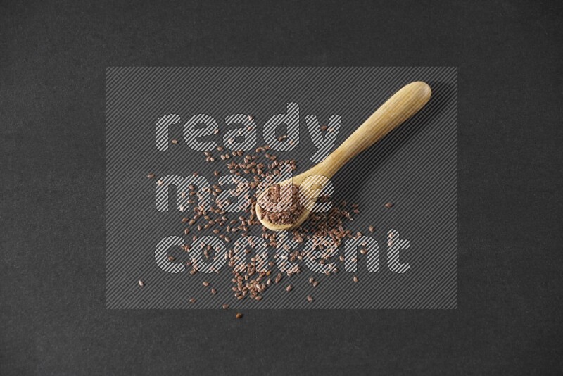 A wooden spoon full of flaxseeds and seeds spread beside it on a black flooring